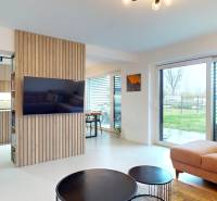 Obývací pokoj s velkými okny, pohodlnou sedačkou a dřevěným dekorem na stěně.