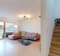 Interiér rodinného domu: pohovka, knihovna, schody s podlahou s dřevěným dekorem a rostlina.