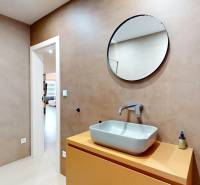 Koupelna v rodinném domě s umyvadlem, kulatým zrcadlem a sprchovým koutem.