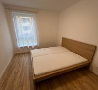 Ložnice s postelí, podlaha s dřevěným dekorem v 2-pokojovém bytě.