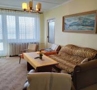 Obývací pokoj s pohovkou, křeslem a stolem v dvoupokojovém bytě s velkým oknem.