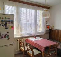 Kuchyně v 2-pokojovém bytě s jídelním stolem, židlemi a lednicí s magnetkami.