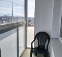 Zasklený balkon s výhledem a plastovou židlí, součást 2-pokojového bytu.