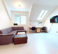 Kanceláře s podlahou s dřevěným dekorem, stůl, sedačka a obrazovka na zdi.