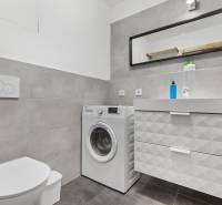 Koupelna s pračkou a umyvadlem, dlažba, skříňka se zásuvkami, zrcadlo v 1-pokojovém bytě.