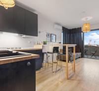 Kuchyně s černými skříňkami, barovým pultem a podlahou s dřevěným dekorem v 1-pokojovém bytě.