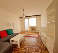 Obývací pokoj v 2-pokojovém bytě s pohovkou, bílým nábytkem, pestrobarevnými polštáři a podlahou s dřevěným dekorem.