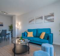 Obývací pokoj v 2-pokojovém bytě s modrou pohovkou a jídelním stolem.