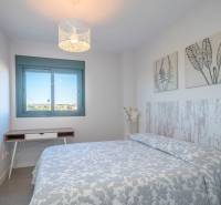 Ložnice v dvoupokojovém bytě se vzorovanou přikrývkou a dekoracemi na stěnách.