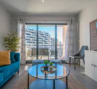 Obývací pokoj v 2-pokojovém bytě s terasou, modrou pohovkou a rostlinou.