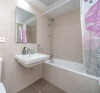 Koupelna v 2-pokojovém bytě s moderními obklady, vanou a umyvadlem.