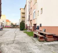 Parkování a lavička před budovou na Hodžově ulici v Trenčíně, blízko 2-pokojového bytu.