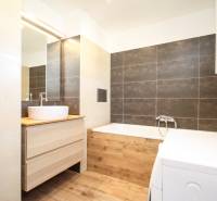 Koupelna se světlými obklady, pračkou a podlahou s dřevěným dekorem v 2-pokojovém bytě.