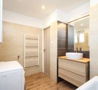 Koupelna v 2-pokojovém bytě s umyvadlem, zrcadlem, pračkou a podlahou s dřevěným dekorem.