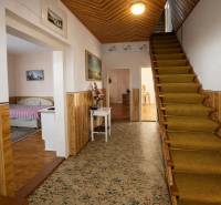 Chodba rodinného domu s kobercem, schody a postelí v další místnosti.