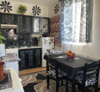 Kuchyně se stoly, černými skříňkami a vzorovanými záclonami v 1-pokojovém bytě.