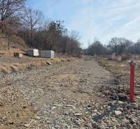 Pozemky - bydlení v Hanisce, kamenitá cesta mezi stromy a kontejner.