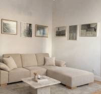 Obývací pokoj v 3-pokojovém bytě s béžovou sedačkou, stolkem, obrazy a podlahou s dřevěným dekorem.