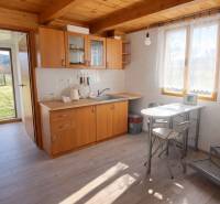 Kuchyně v chatě s dřevěným dekorem a nábytkem, slunečné prostředí.