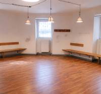 Obchodní prostory se stěnami, lavicemi a podlahou s dřevěným dekorem, osvětlené závěsnými lampami.