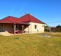 Rodinný dům v Zemianské Olči s červenou střechou a dřevěným přístřeškem, travnatá zahrada.