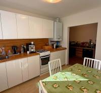 Kuchyně v rodinném domě s bílými skříňkami, dřevěným dekorem a jídelním stolem.