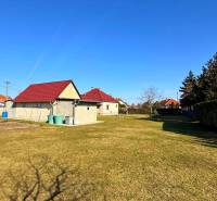 Travnatý pozemek u rodinného domu v Zemianské Olči s několika domy a keři.