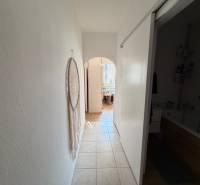 Chodba s dlažbou v 3-pokojovém bytě s dekorací na stěně a pohledem do koupelny.