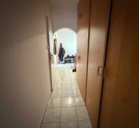 Úzká chodba s dlažbou a vestavěnými skříněmi vedoucí do obývací části 3pokojového bytu.