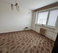 Pokoj v 1-pokojovém bytě s oknem, bílými stěnami a podlahou s dřevěným dekorem.