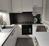 Kuchyně s bílými skříňkami a stolem v 2-pokojovém bytě s podlahou s dřevěným dekorem.