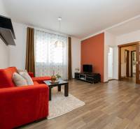 Obývací pokoj v 2-pokojovém bytě s pohovkou, TV, podlahou s dřevěným dekorem a dekorativními závěsy.