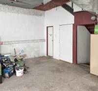 Garáž v rodinném domě, uložené nářadí, betonová podlaha, schody a bílý nábytek.