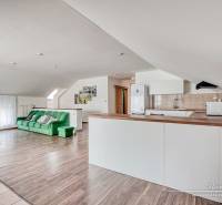 Obývací pokoj s kuchyní, zelená sedačka, bílý nábytek, podlaha s dřevěným dekorem.