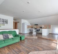 Interiér rodinného domu s pohovkou, kuchyňským koutem a podlahou s dřevěným dekorem.