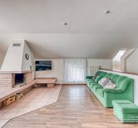 Obývací pokoj v rodinném domě s krbem, zelenou sedačkou a podlahou s dřevěným dekorem.