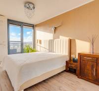 Ložnice v 3pokojovém bytě s postelí, komodou, dekoracemi a podlahou s dřevěným dekorem.