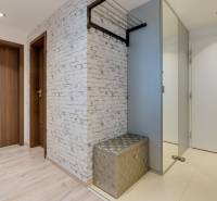 Chodba s podlahou s dřevěným dekorem, bílou stěnou a lesklou lavicí v 3-pokojovém bytě.