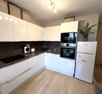 Kuchyně v 2-pokojovém bytě s bílými skříňkami, spotřebiči a podlahou s dřevěným dekorem.