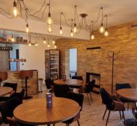 Gastro prostory s visícími světly, dřevěným dekorem a útulným sezením.