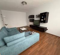 Obývací pokoj s televizí, modrou sedačkou a podlahou s dřevěným dekorem ve 3-pokojovém bytě.