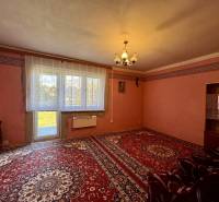 Obývací pokoj v rodinném domě s červeným kobercem, jednoduchými záclonami a světlem.