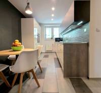 Kuchyně v 2pokojovém bytě s jídelním stolem, dlažbou a světly nad pracovní deskou.