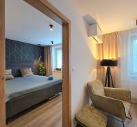 Dvoupokojový byt s podlahou s dřevěným dekorem zahrnuje ložnici, křeslo a lampu.