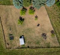 Letecký pohled na pozemek určený k bydlení v Banské Belé s travnatou plochou a stromy.