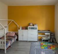 Dětský pokoj s postelí, komodou, klavírem, hračkami a podlahou s dřevěným dekorem ve 2-pokojovém bytě.