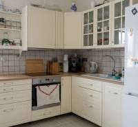 Kuchyně v 2-pokojovém bytě s bílými skříňkami a spotřebiči, podlaha s dřevěným dekorem.