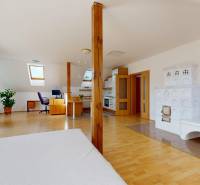 Podkrovní interiér rodinného domu s kachlovými kamny, pracovním koutem a podlahou s dřevěným dekorem.