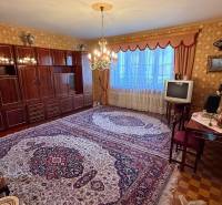 Obývací pokoj v rodinném domě s kobercem, starší televizí a elegantním lustrem.