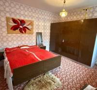 Ložnice v rodinném domě s kobercem, vzorovanou tapetou a velkou skříní.